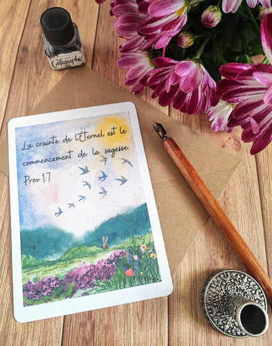 Carte postale aquarelle représentant un champ de fleurs aux couleurs vives avec des collines verdoyantes à l'arrière-plan et des oiseaux s'envolant dans un ciel bleu azur. Le verset biblique Proverbes 1:7 